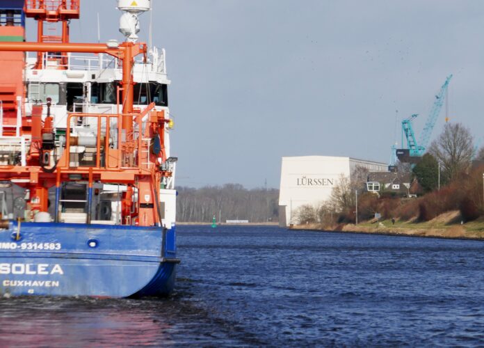 Ein Schiff auf dem Nord-Ostsee-Kanal, rechts das Gebäude der Werft